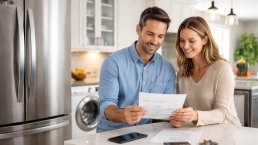 hands holding a receipt and a small appliance with a warranty card on a wooden table