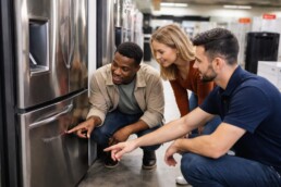 appliance sales associate showing a scratched refrigerator to a middle-aged couple in a modern showroom